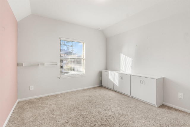 unfurnished room with light carpet, vaulted ceiling, and baseboards