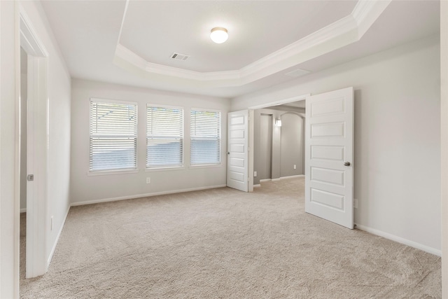 spare room featuring carpet floors, visible vents, baseboards, ornamental molding, and a raised ceiling