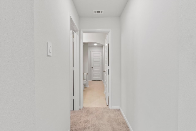 corridor with light carpet, arched walkways, visible vents, and baseboards