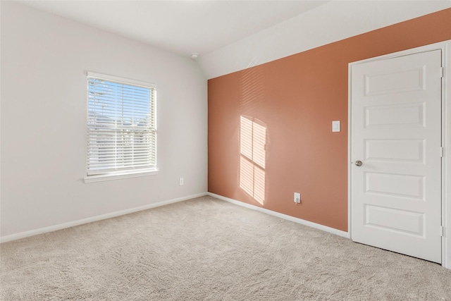 carpeted spare room featuring vaulted ceiling and baseboards