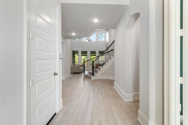 foyer featuring light wood-style floors, stairs, baseboards, and arched walkways