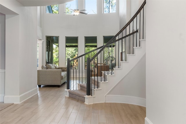 entryway featuring a ceiling fan, a towering ceiling, baseboards, and wood finished floors