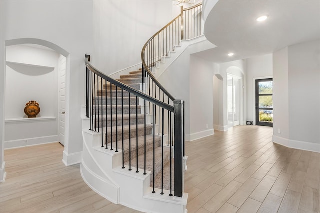 staircase with a towering ceiling, baseboards, wood finished floors, and recessed lighting