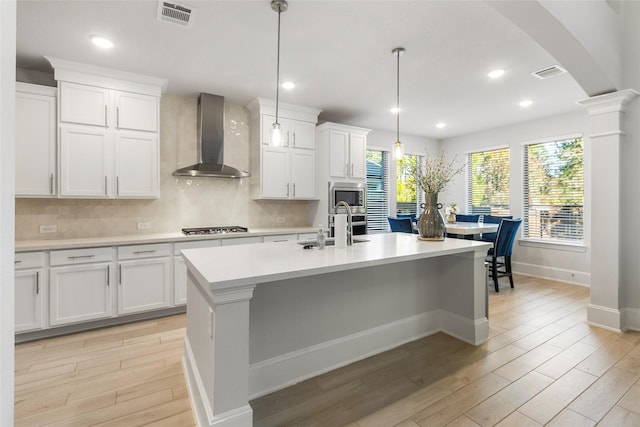 kitchen featuring wall chimney exhaust hood, appliances with stainless steel finishes, visible vents, and arched walkways