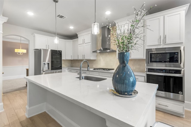 kitchen featuring a sink, visible vents, light wood-style floors, appliances with stainless steel finishes, and wall chimney range hood