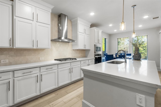 kitchen with visible vents, white cabinets, wall chimney exhaust hood, stainless steel appliances, and a sink