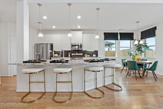 kitchen with a center island with sink, white cabinets, light hardwood / wood-style flooring, light stone countertops, and stainless steel appliances