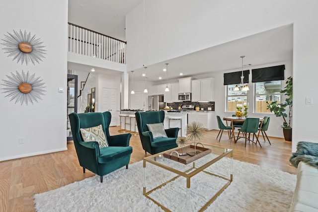 living room featuring light hardwood / wood-style floors, a towering ceiling, and an inviting chandelier