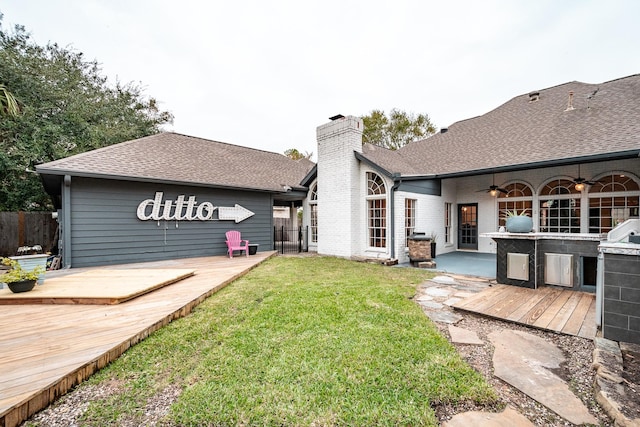 back of property with a lawn, ceiling fan, a wooden deck, and an outdoor kitchen