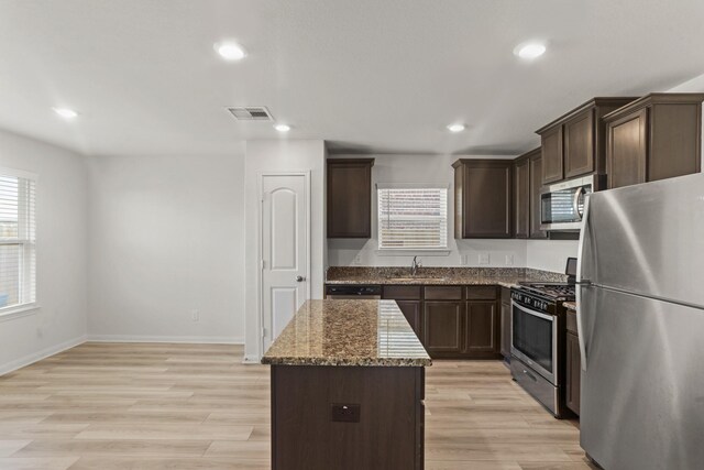 kitchen featuring light wood-type flooring, light stone counters, stainless steel appliances, sink, and a kitchen island