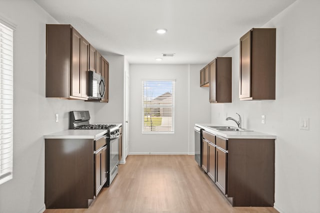 kitchen with dark brown cabinetry, sink, stainless steel appliances, and light hardwood / wood-style flooring