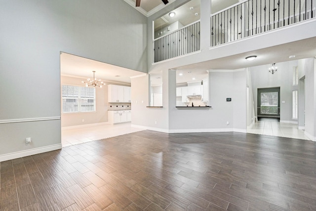 unfurnished living room featuring a high ceiling, ceiling fan with notable chandelier, hardwood / wood-style flooring, and crown molding