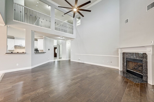 unfurnished living room featuring a towering ceiling, ceiling fan, dark wood-type flooring, and a premium fireplace