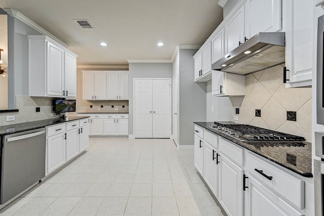 kitchen with tasteful backsplash, ornamental molding, stainless steel appliances, dark stone countertops, and white cabinets