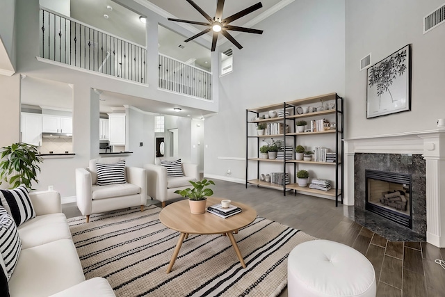 living room featuring dark wood-type flooring, ceiling fan, ornamental molding, a towering ceiling, and a fireplace