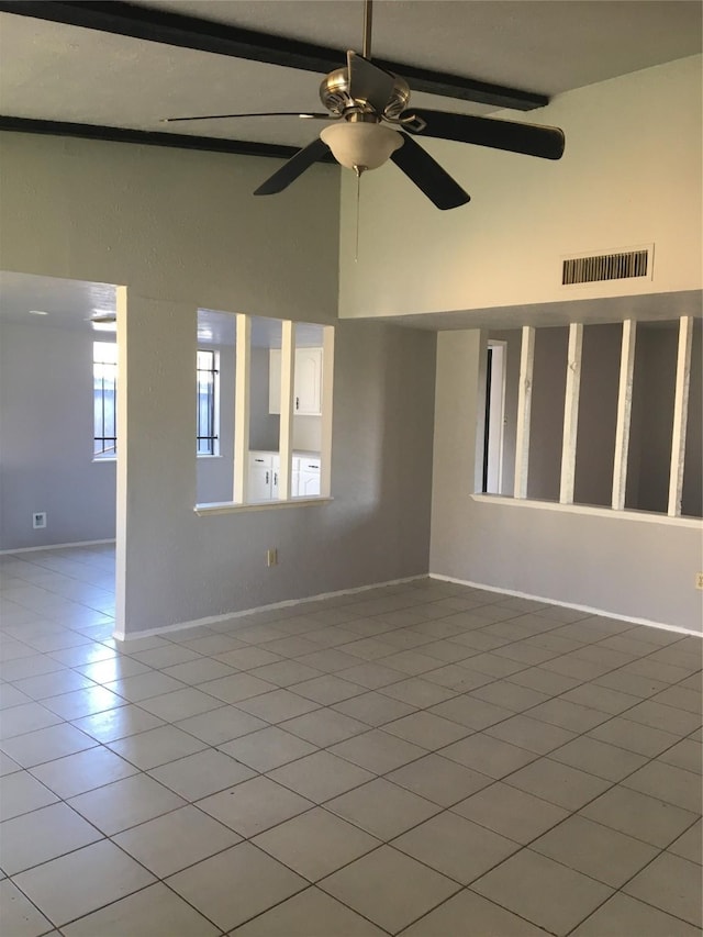 empty room featuring beamed ceiling, ceiling fan, light tile patterned flooring, and a towering ceiling