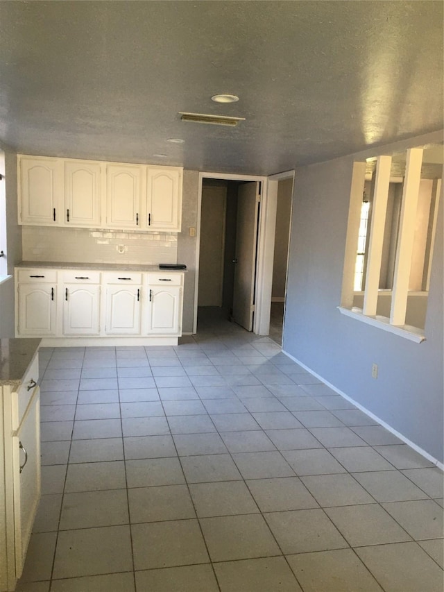 kitchen featuring white cabinets, decorative backsplash, light tile patterned floors, and a textured ceiling