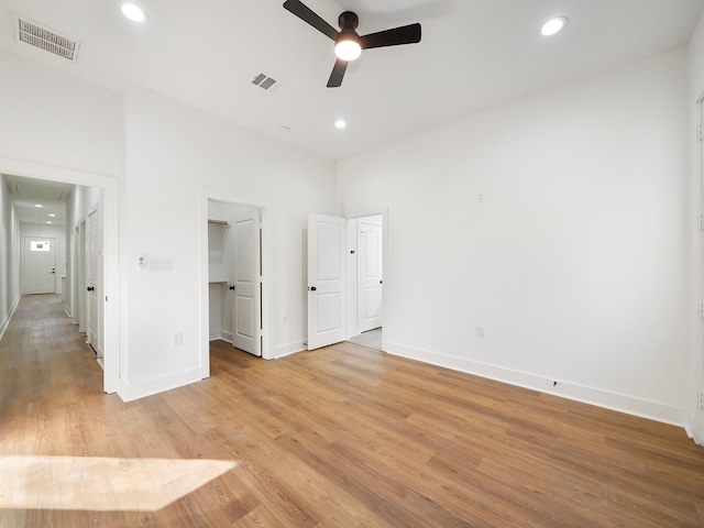 unfurnished bedroom with a walk in closet, light wood-type flooring, a closet, and ceiling fan