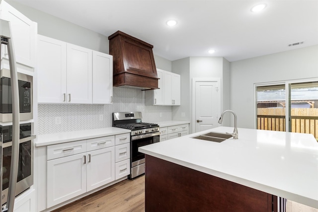 kitchen featuring light wood-type flooring, custom exhaust hood, stainless steel appliances, sink, and white cabinets