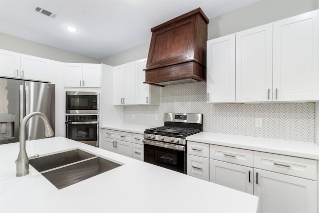 kitchen featuring decorative backsplash, custom range hood, stainless steel appliances, sink, and white cabinetry