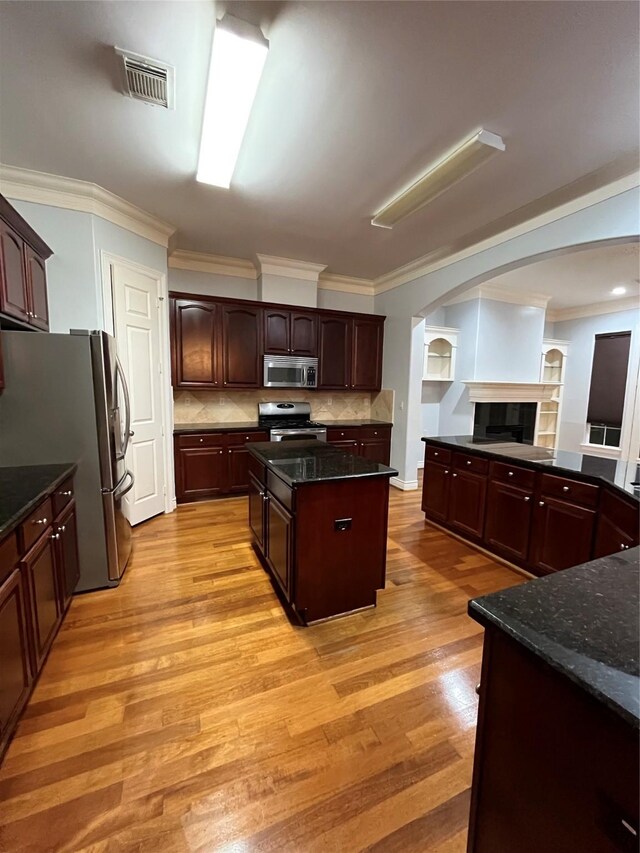 kitchen featuring crown molding, dark stone countertops, stainless steel appliances, a center island, and decorative backsplash