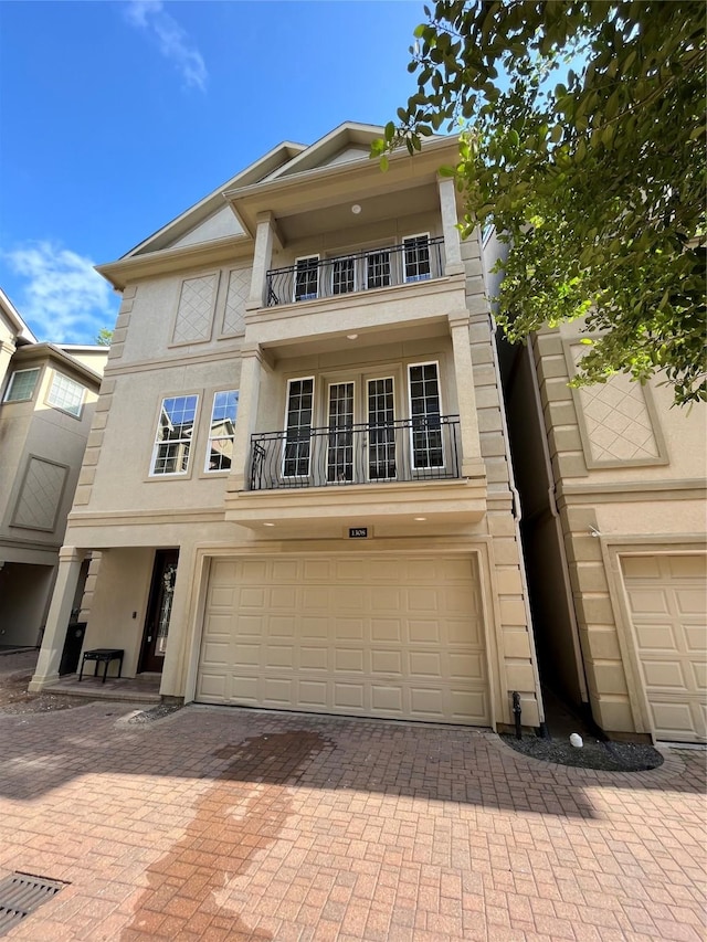 view of front facade with stucco siding, decorative driveway, a balcony, and an attached garage