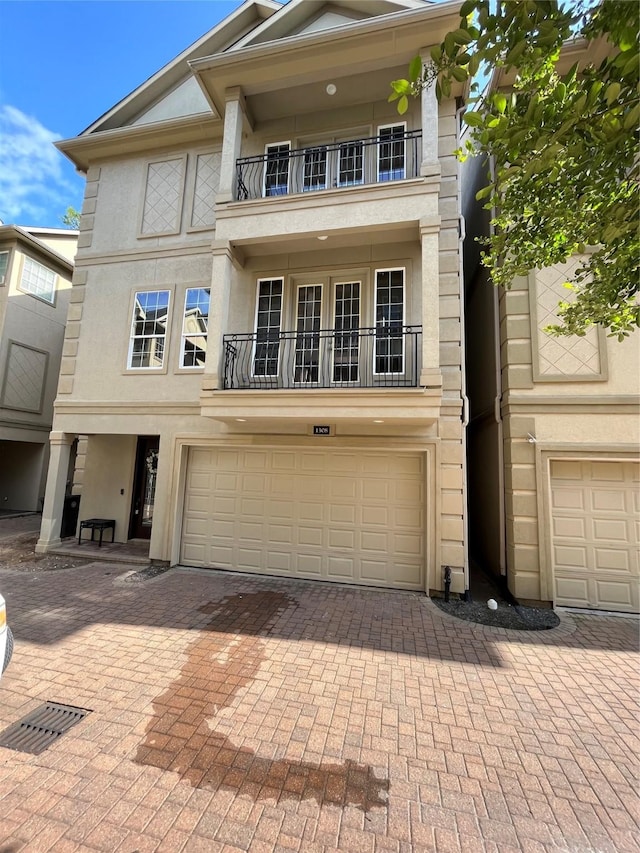 view of front facade with stucco siding, decorative driveway, a balcony, and a garage