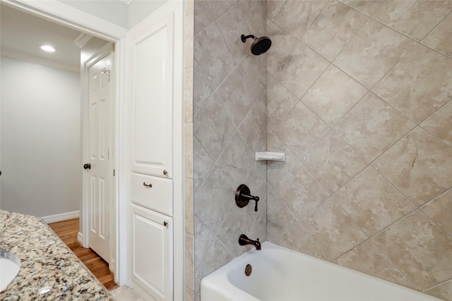 bathroom with tiled shower / bath combo, wood-type flooring, ornamental molding, and vanity