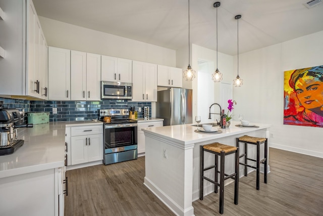 kitchen featuring dark wood-type flooring, white cabinetry, a center island with sink, and stainless steel appliances