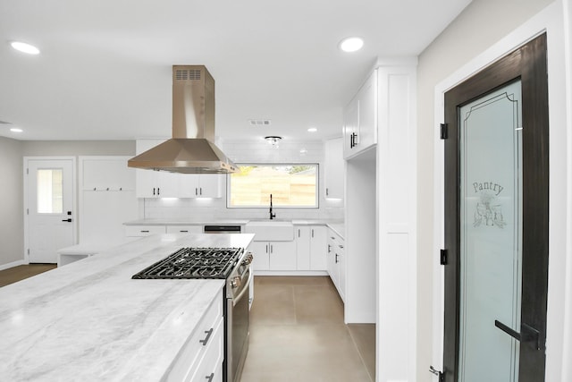 kitchen with white cabinetry, stainless steel gas range oven, light stone counters, and range hood