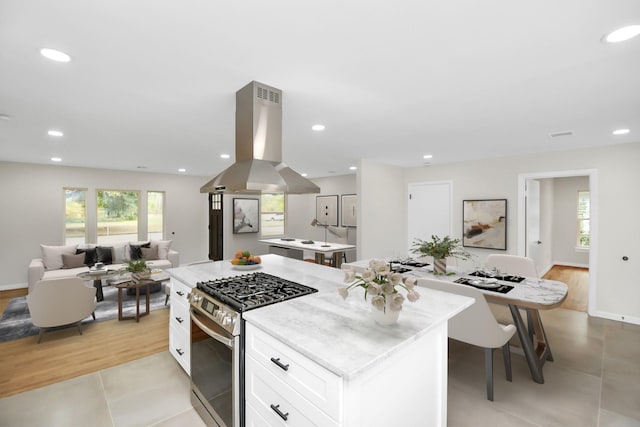 kitchen featuring island exhaust hood, white cabinets, a center island, light hardwood / wood-style floors, and stainless steel range with gas cooktop