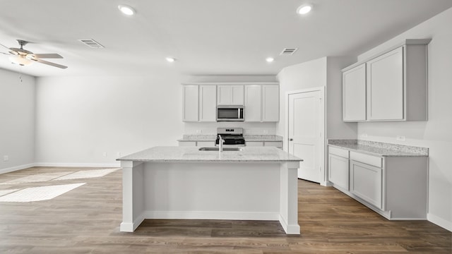 kitchen featuring hardwood / wood-style floors, light stone countertops, appliances with stainless steel finishes, sink, and a center island with sink