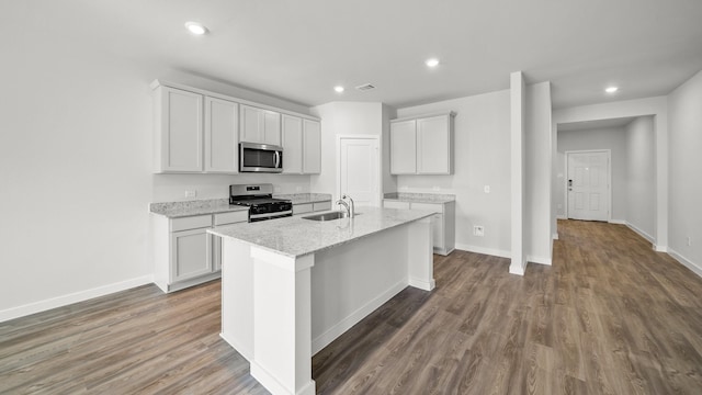 kitchen with stainless steel appliances, white cabinetry, light stone countertops, and an island with sink