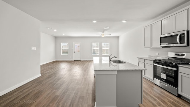 kitchen with appliances with stainless steel finishes, sink, hardwood / wood-style flooring, light stone countertops, and a center island with sink