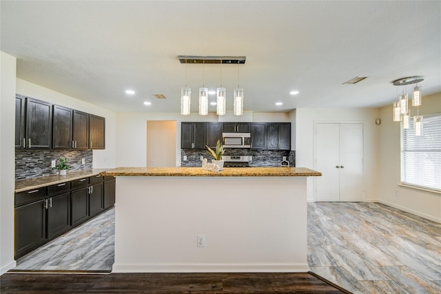 kitchen featuring appliances with stainless steel finishes, light hardwood / wood-style floors, hanging light fixtures, and an island with sink