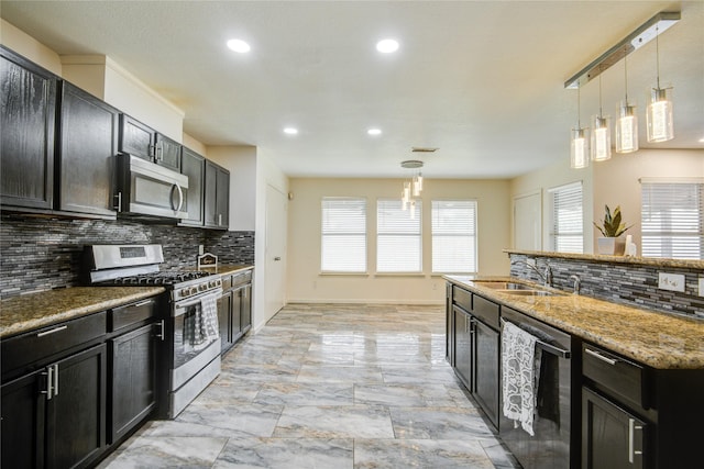 kitchen with appliances with stainless steel finishes, backsplash, sink, decorative light fixtures, and dark stone countertops