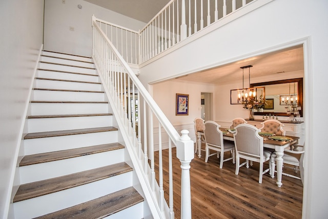 staircase with hardwood / wood-style floors, ornamental molding, and a notable chandelier