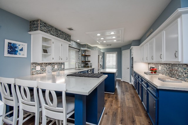 kitchen with kitchen peninsula, blue cabinetry, dark hardwood / wood-style floors, white cabinetry, and a breakfast bar area