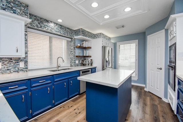 kitchen featuring appliances with stainless steel finishes, blue cabinets, dark wood-type flooring, white cabinets, and a kitchen island