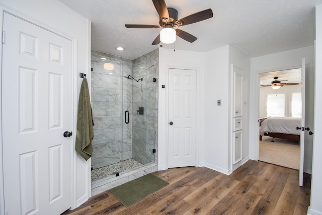 bathroom with hardwood / wood-style flooring, ceiling fan, a shower with shower door, and a textured ceiling