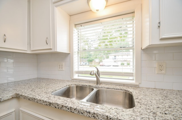 kitchen with decorative backsplash, light stone counters, white cabinetry, and sink