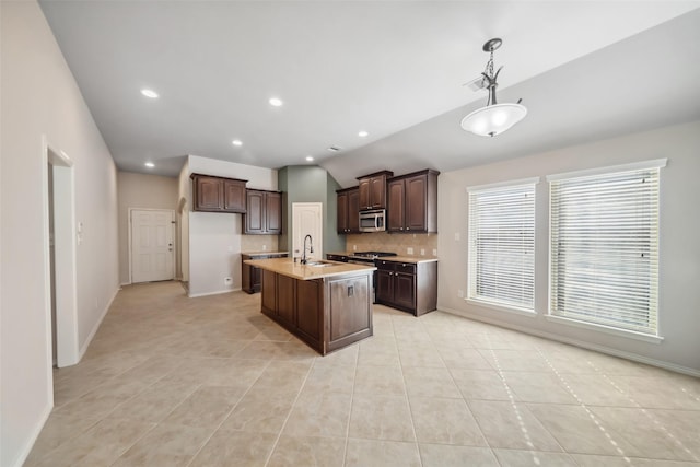 kitchen featuring a center island with sink, sink, hanging light fixtures, appliances with stainless steel finishes, and dark brown cabinetry