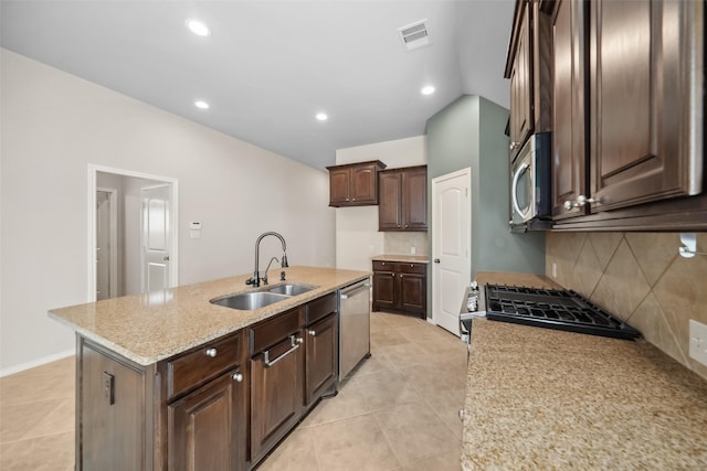 kitchen featuring appliances with stainless steel finishes, light stone counters, dark brown cabinetry, a kitchen island with sink, and sink