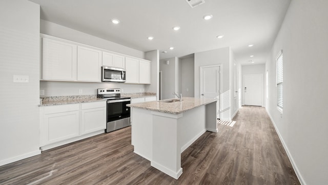 kitchen with white cabinets, a center island with sink, dark hardwood / wood-style floors, appliances with stainless steel finishes, and light stone counters