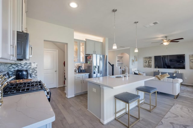 kitchen with a center island with sink, hanging light fixtures, sink, decorative backsplash, and appliances with stainless steel finishes