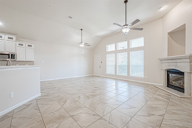 unfurnished living room with ceiling fan, light tile patterned floors, and vaulted ceiling