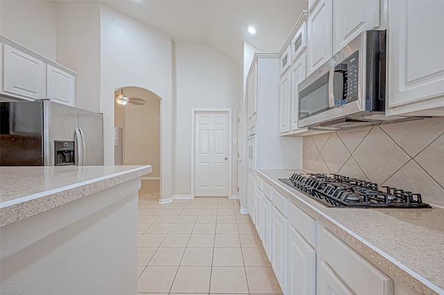 kitchen featuring appliances with stainless steel finishes, backsplash, light tile patterned floors, high vaulted ceiling, and white cabinetry