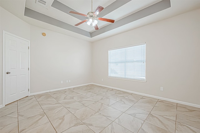 empty room with ceiling fan and a raised ceiling