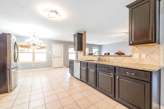 kitchen featuring light stone countertops, sink, backsplash, a chandelier, and appliances with stainless steel finishes