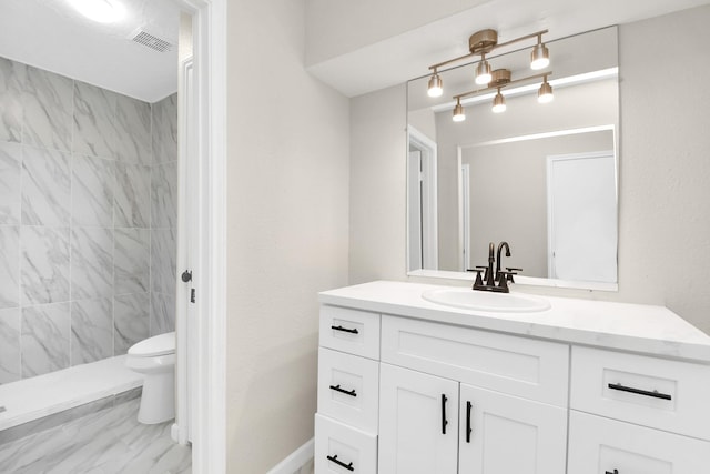 bathroom with tiled shower, vanity, and toilet